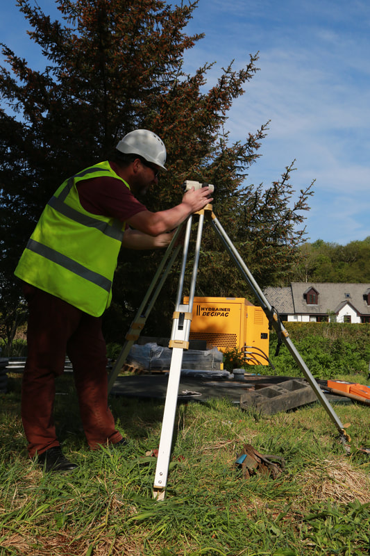 A dumpy level being used to on a tripod with houses and a blue sky in the background