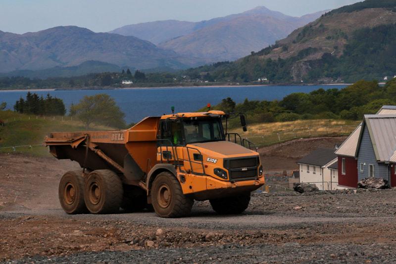 A yellow articulated dump truck on site with the sea in the background