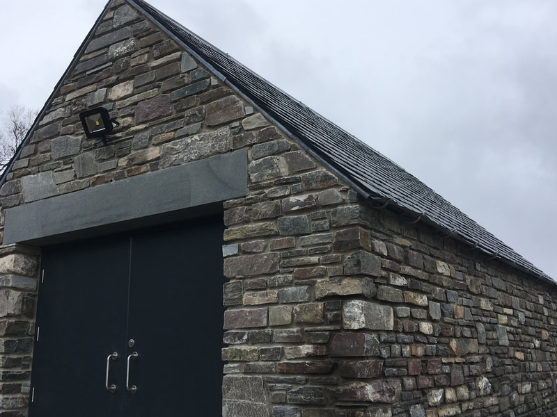 A stone building showing the gable end, grey double doors, and a slate roof 