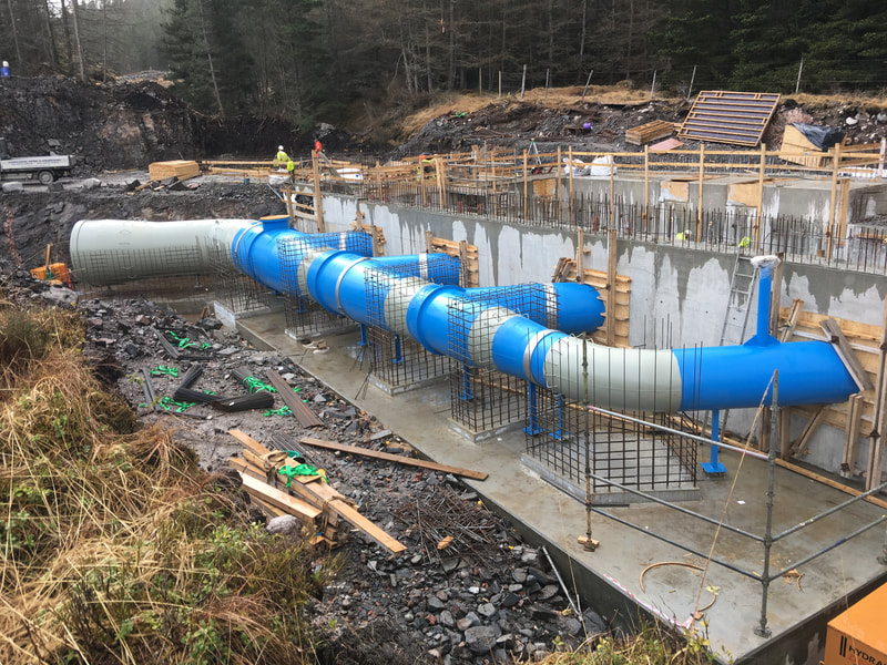 An inlet manifold consisting of a blue steel pipe with 4 offlets set into the concrete. Re bar is visible in several places - this is for the later construction of thrust blocks to support the pipe
