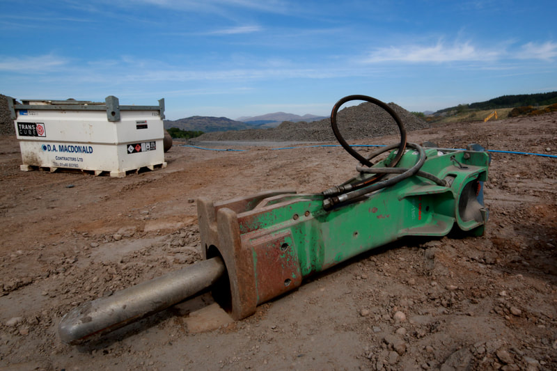 A green breaker attachment for going on the end of diggers, with a fuel bowser behind it